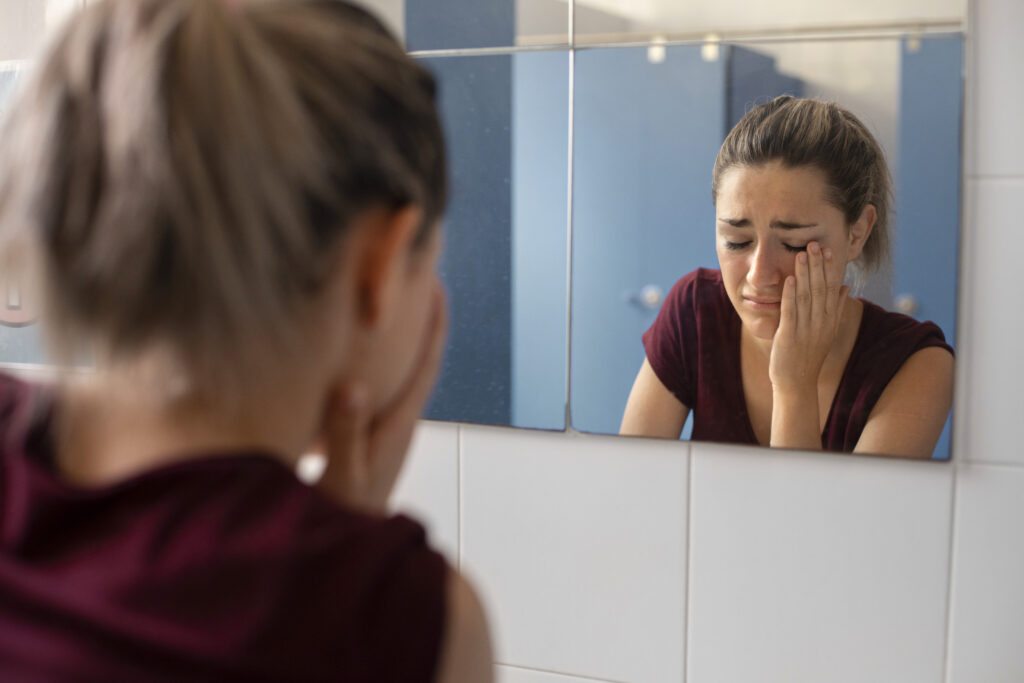 Mulher triste se olhando no espelho sem notar mudanças no corpo após meses de treino