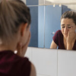 Mulher triste se olhando no espelho sem notar mudanças no corpo após meses de treino